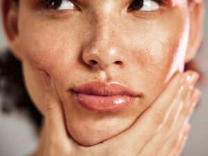 Woman with dewy skin holding her face, showcasing the effects of the proper skincare routine order.