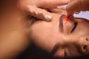 Wax technician applying wax under a client’s eyebrow, shaping the brow for a clean appearance.