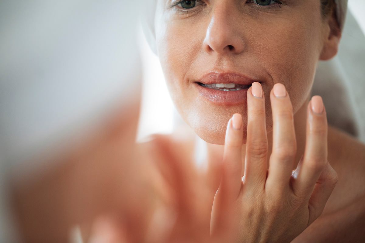 A close-up of a woman touching her lips in front of a mirror, highlighting the application of lip balm for hydration and protection.