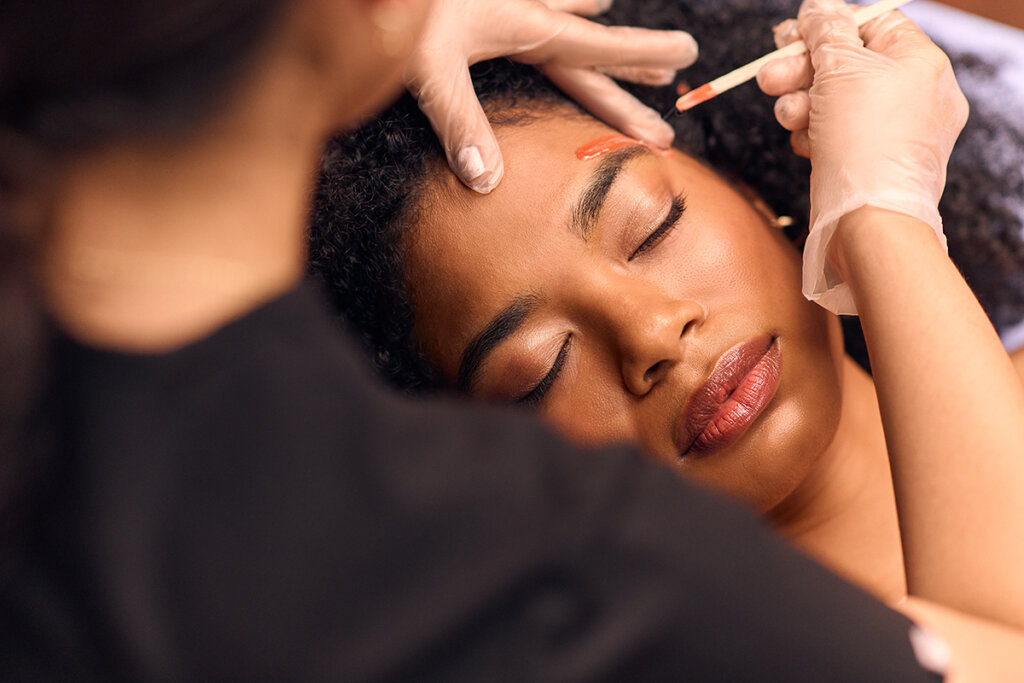 Cerologist performing an eyebrow waxing service on a client.
