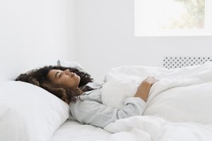 Woman sleeping on her back in a bright, white bedroom after a lash lift.
