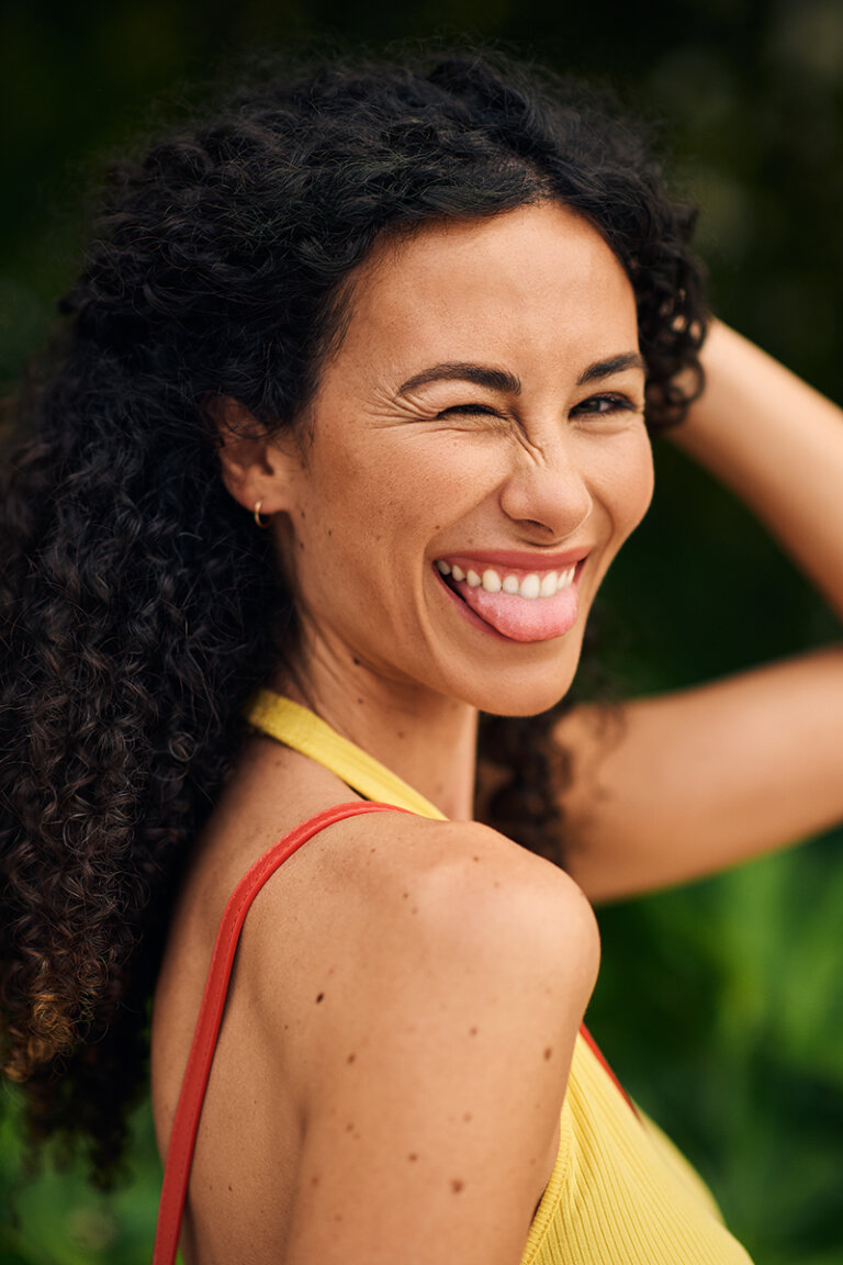 Woman with dark hair in a yellow tank top winks and smiles at the camera.