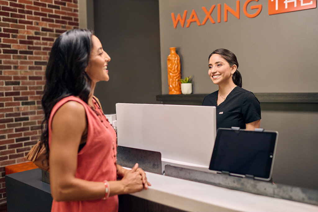 A woman is talking to a Waxing the City specialist at the front desk to schedule her next service appointment.