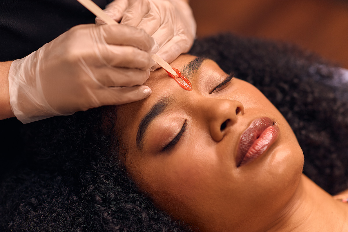 A woman is closing her eyes while laying down and getting her brows professionally waxed.
