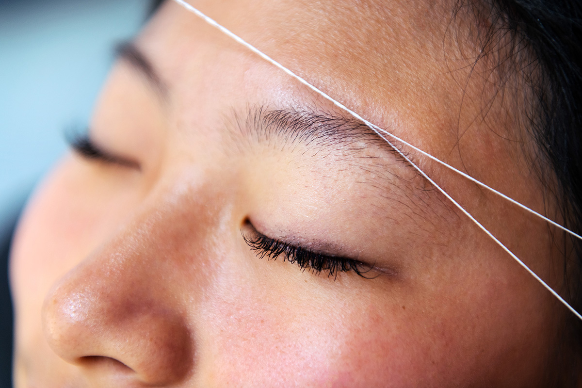 A woman is closing her eyes while her eyebrows are being threaded.