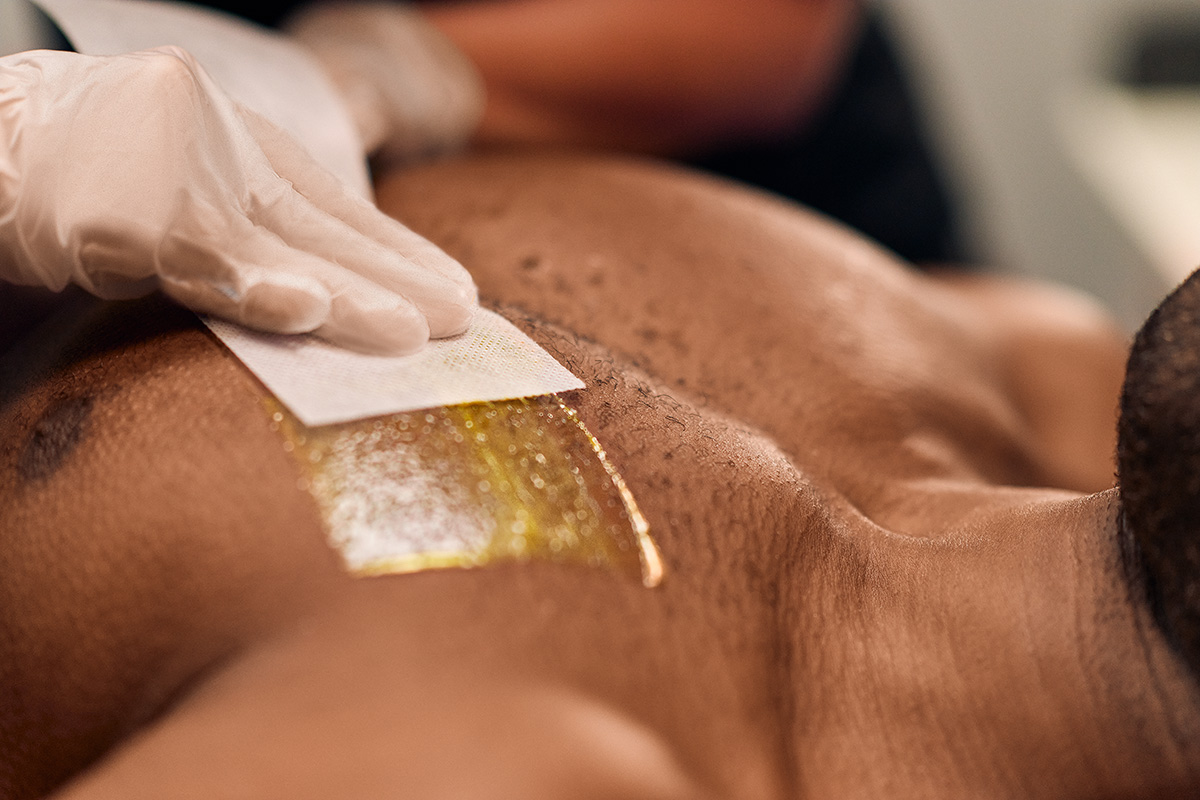 Man receiving a chest wax in a studio setting. A Cerologist is applying a waxing strip with sterile gloves to minimize bumps after waxing.