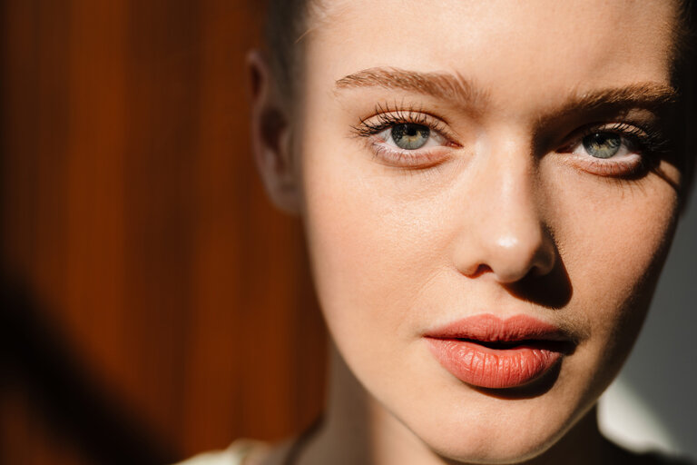 Close-up of a woman with green eyes and long, dark eyebrows in a shadowy room.