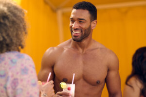 A shirtless man has his chest waxed and is socializing and enjoying a beverage.